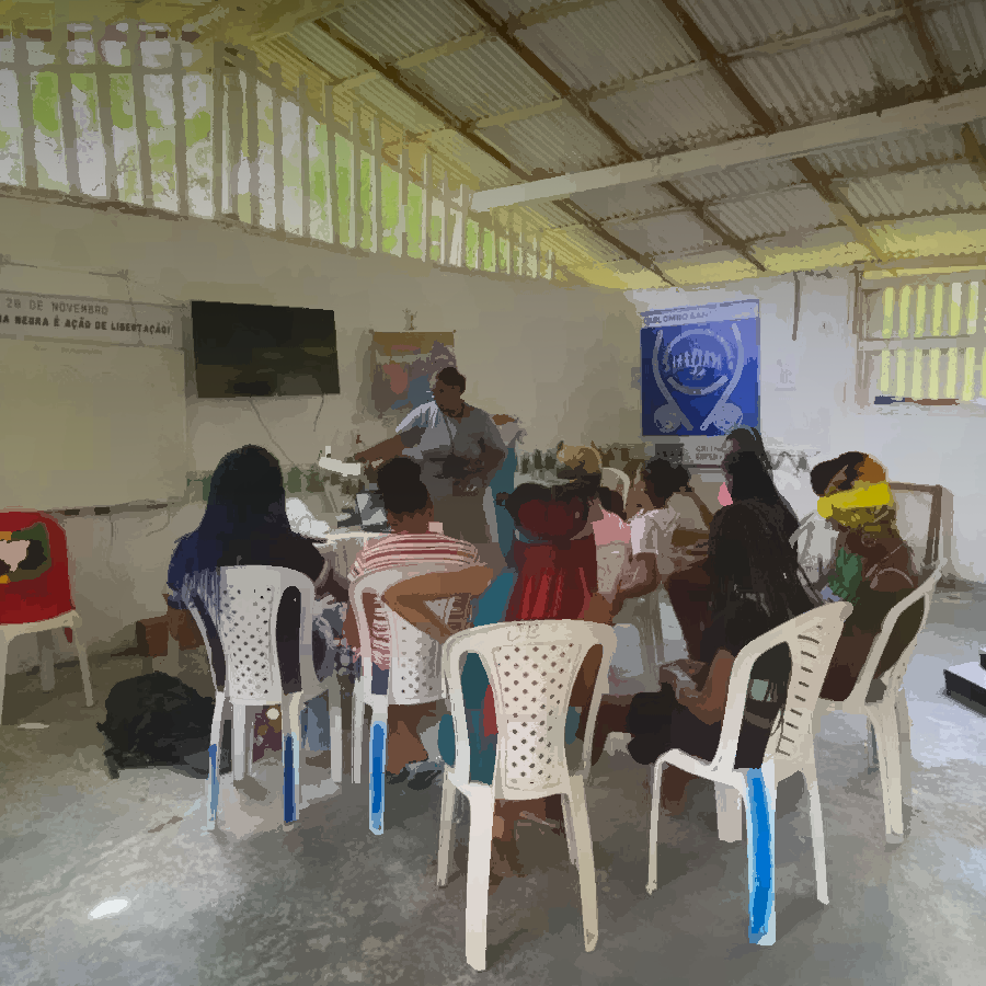 Podemos ver um grupo de pessoas reunidas em um espaço comunitário, para uma oficina.