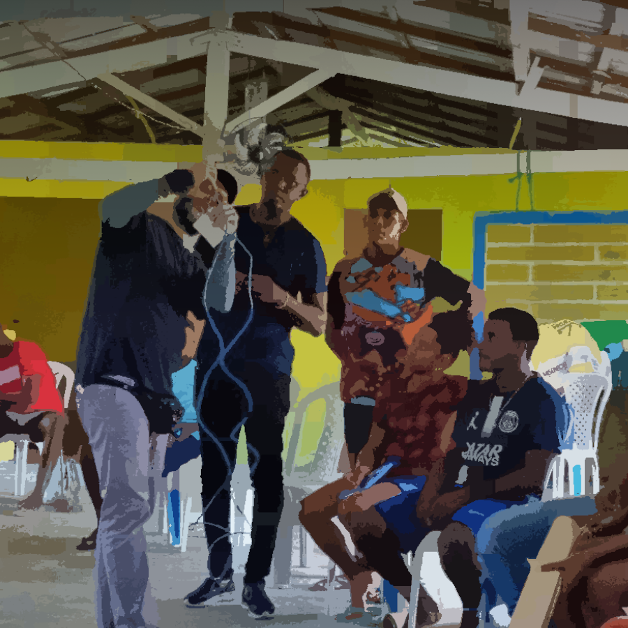 Podemos ver um grupo de pessoas reunidas em um espaço comunitário, observando como é confeccionado um cabo de rede.